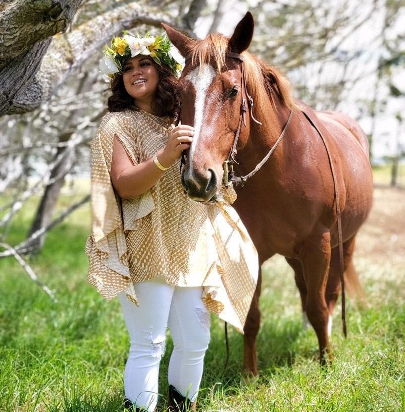 A woman wearing a flower crown stands next to a brown horse