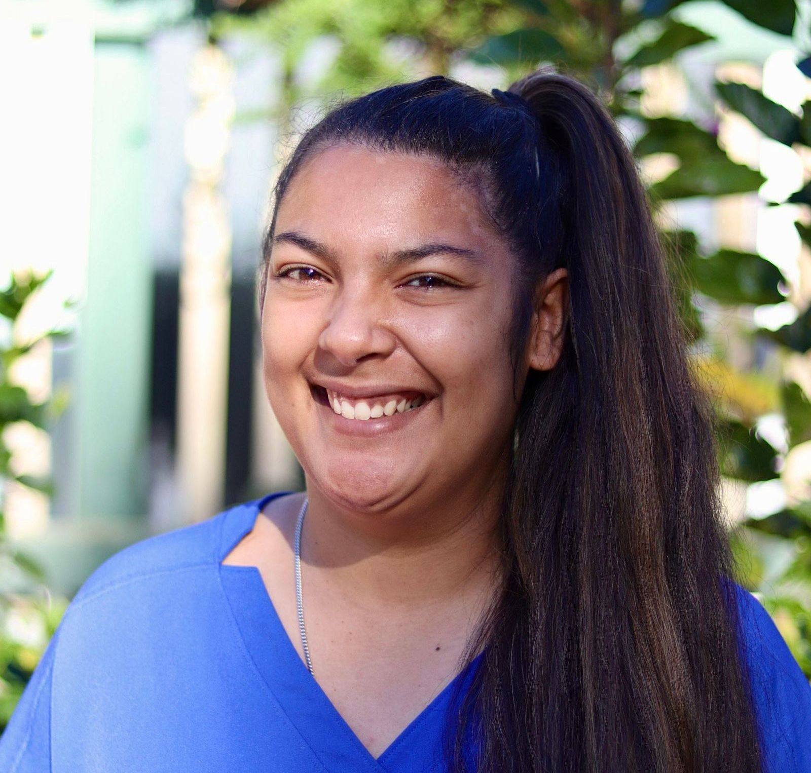 A woman in a blue scrub top is smiling for the camera.