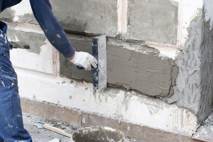 Person using a trowel to apply mortar on a concrete surface, construction work.