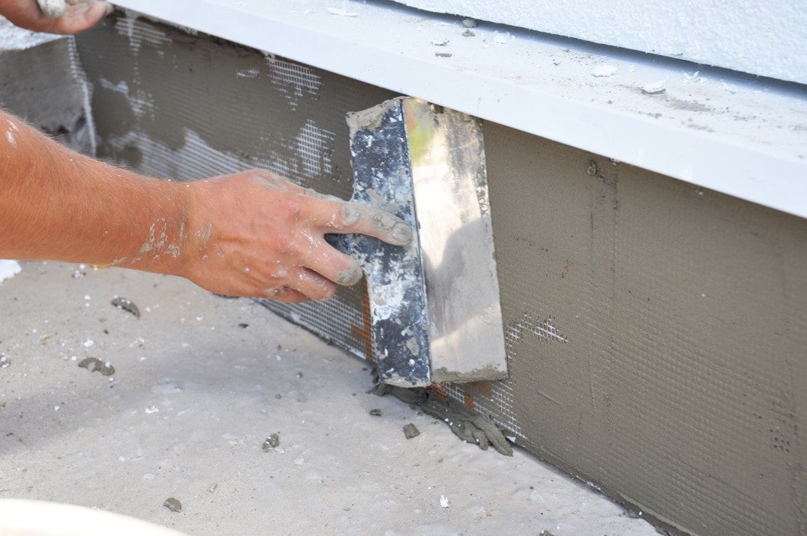Person applying stucco to a wall, using a trowel to smooth the wet material.