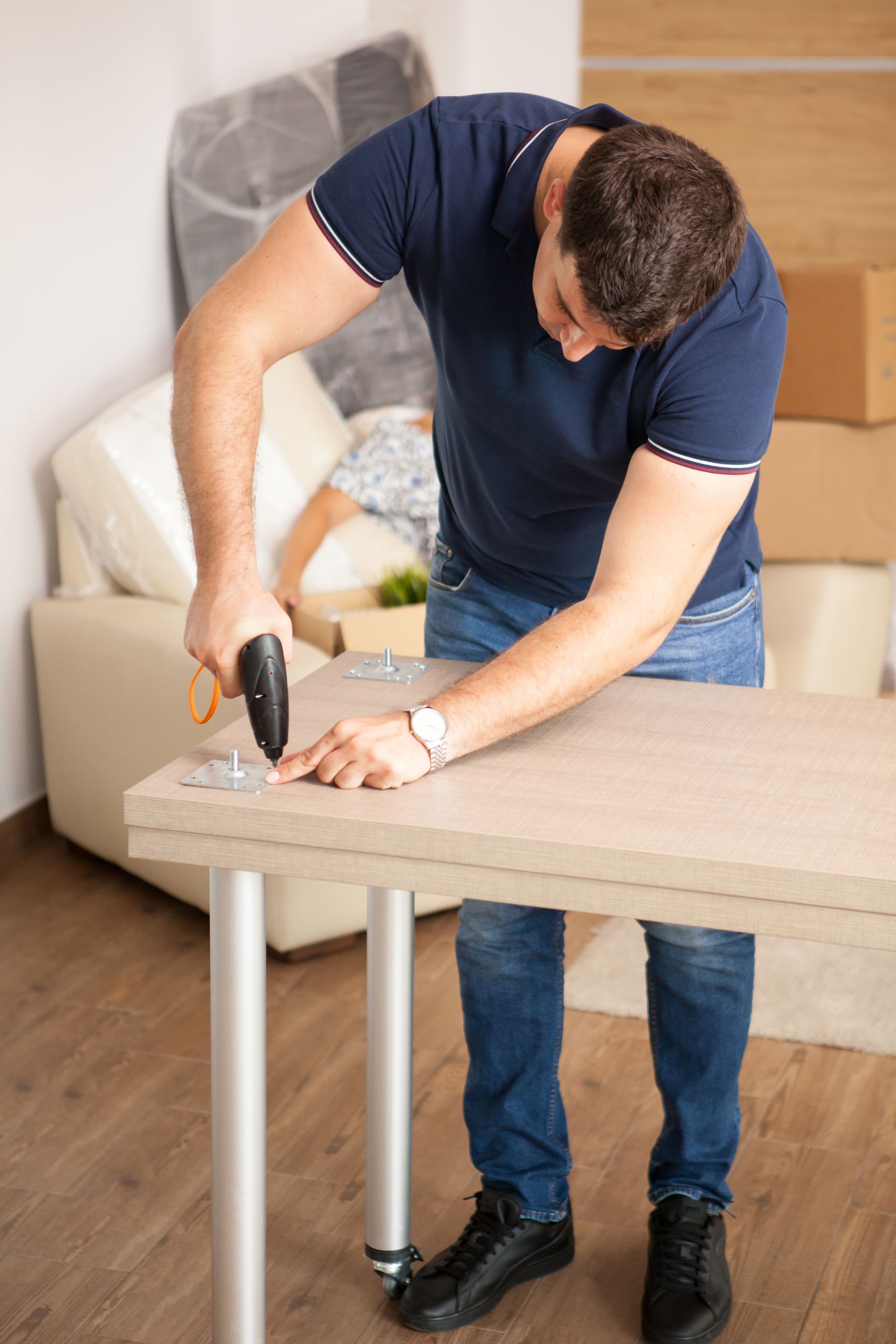A man is using a drill to fix a table in a living room.