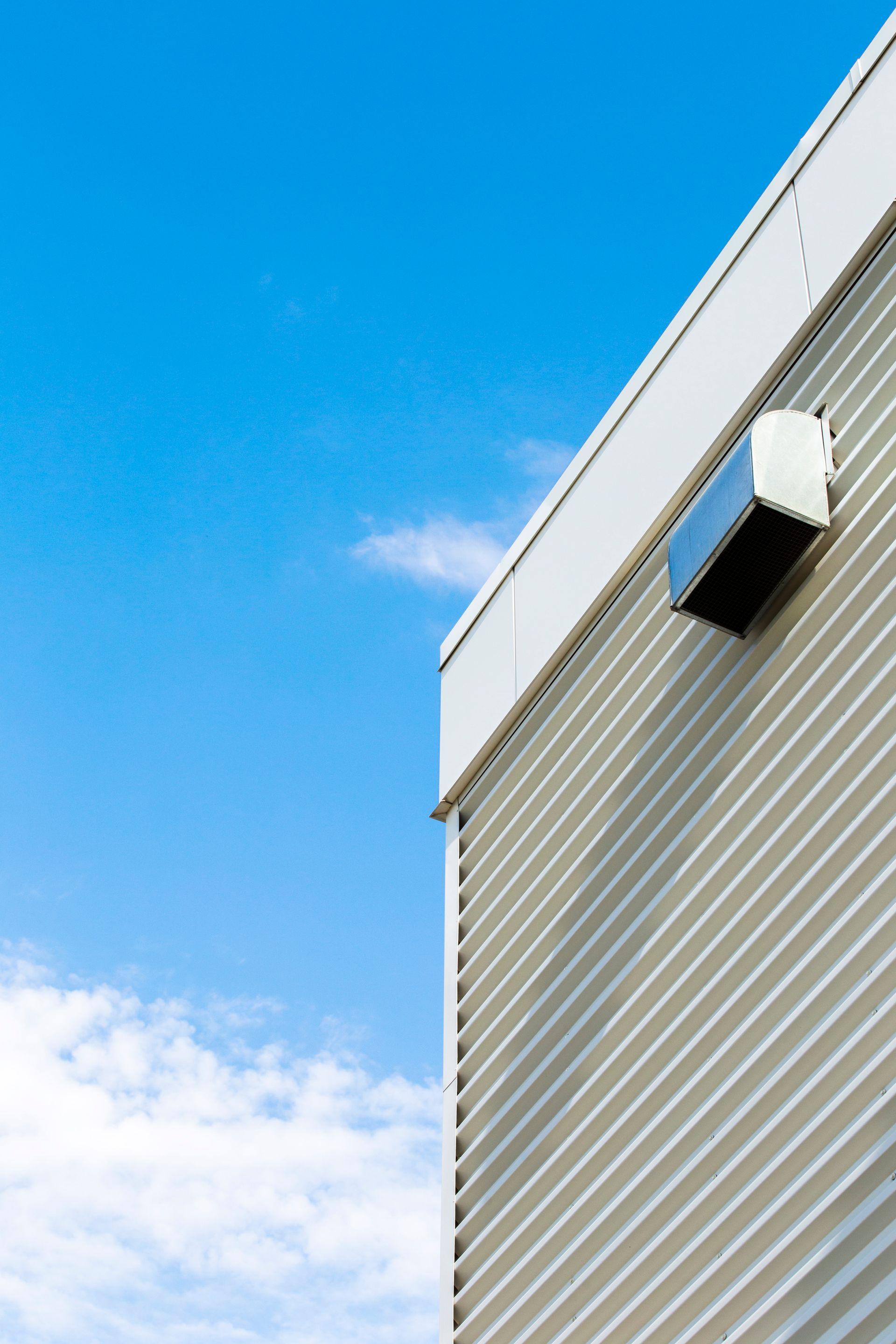 Modern building corner with a gray facade and a small wall-mounted fixture against a blue sky