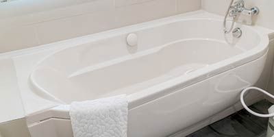A white bathtub is sitting in a bathroom next to a trash can.