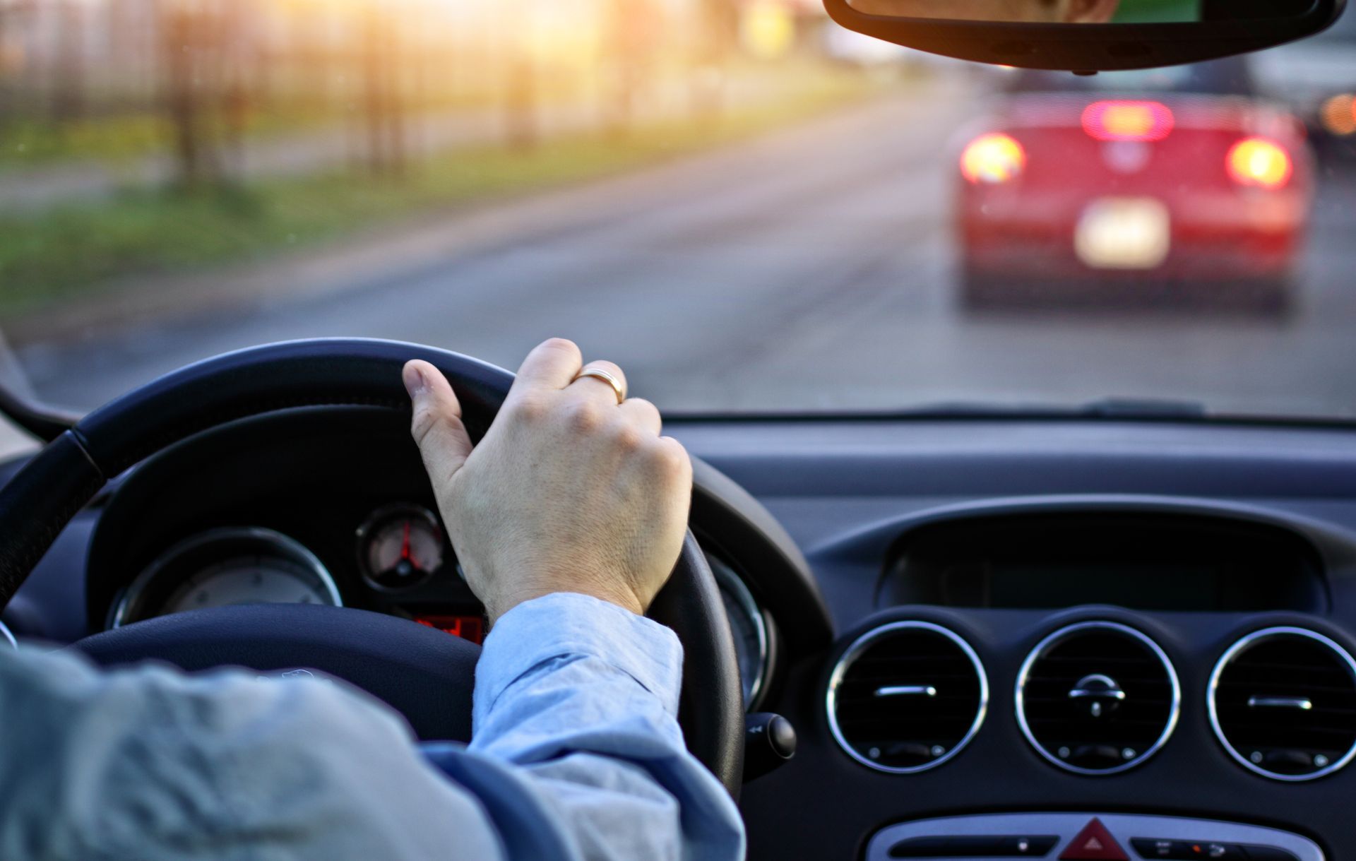Hand on steering wheel, driving a car on a road, following a red car.