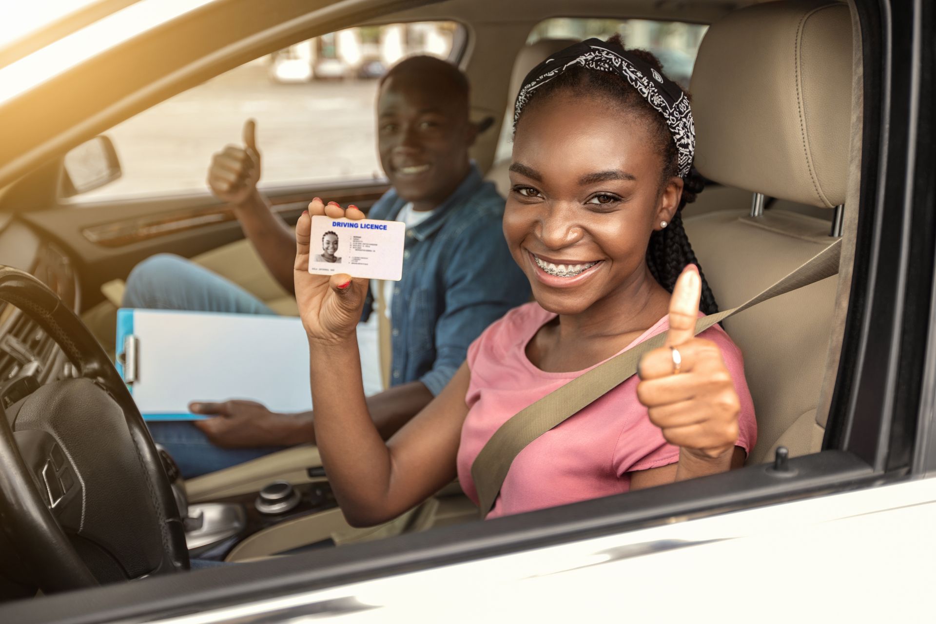 Woman in car, smiling, holding driver's license, giving thumbs up. 