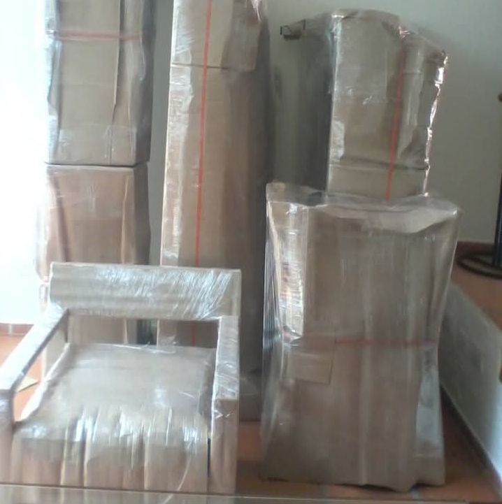 Cajas de cartón envueltas en papel plateado apiladas en el suelo, incluyendo un pequeño paquete con forma de silla en la parte delantera.