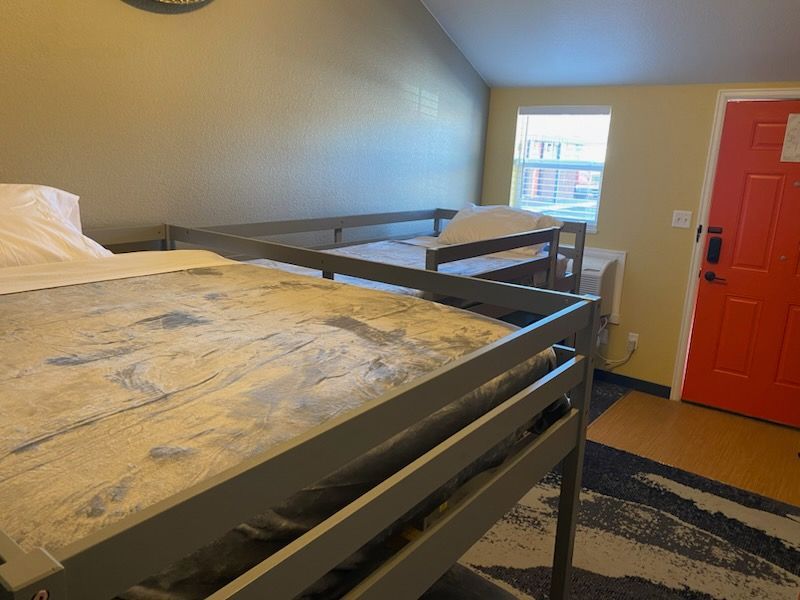 Bunk beds in a room, with a red door and a window. Light beige walls and patterned rug.