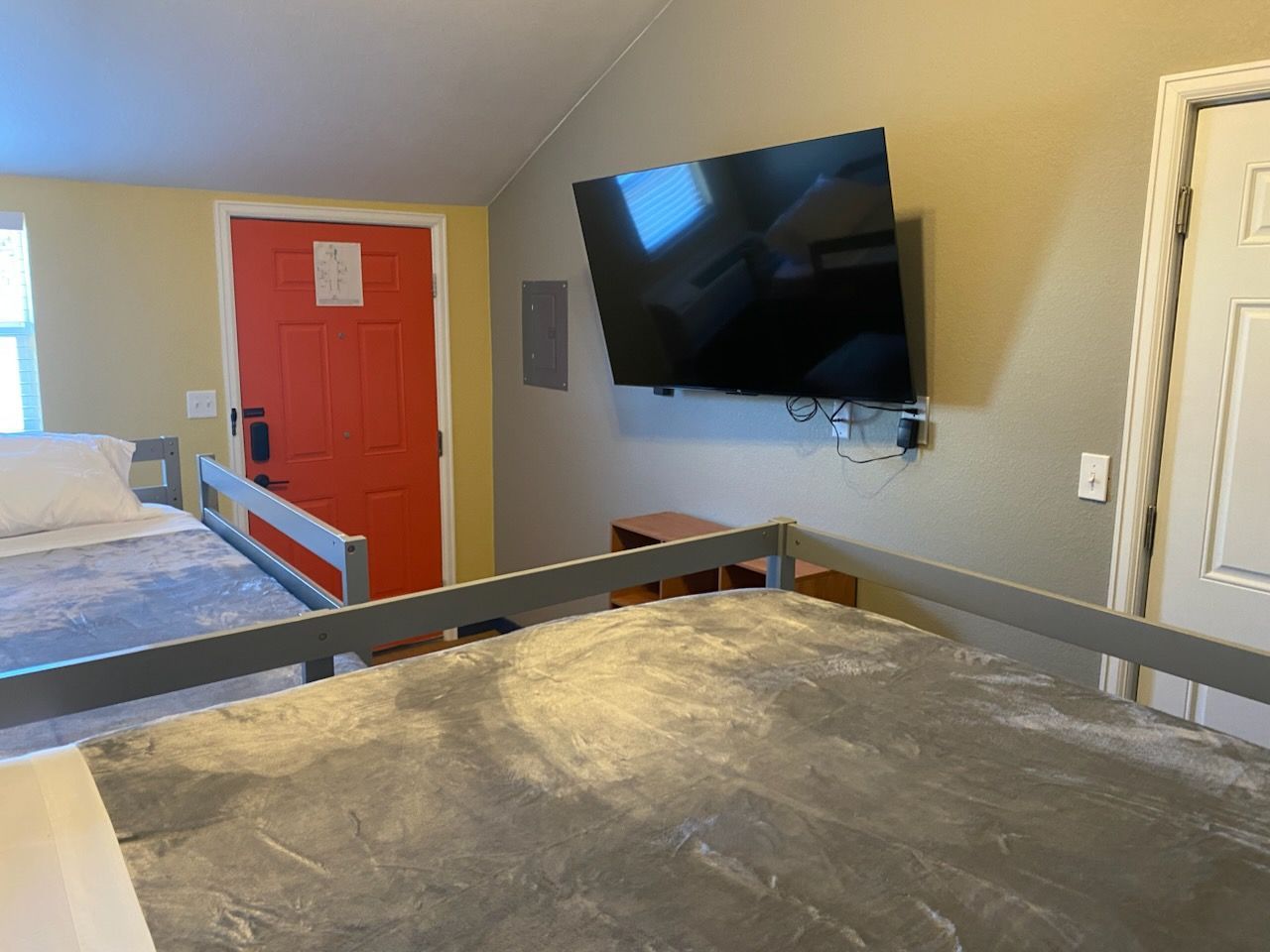 Interior of a room with a bunk bed and a TV mounted on a wall. A red door is visible.