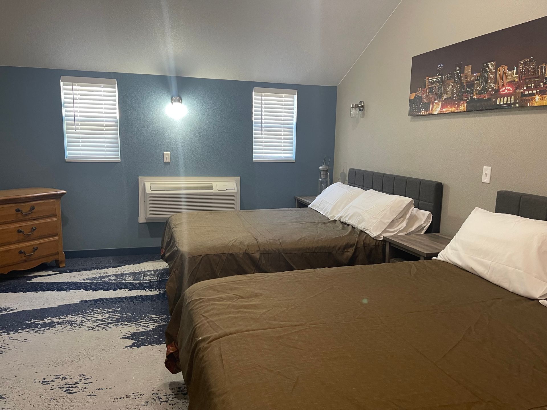 Hotel room with two beds, blue walls, two windows, and a dresser.