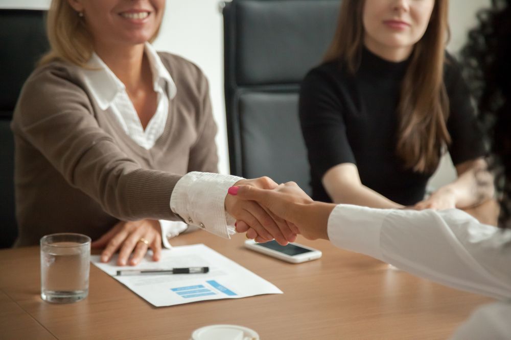 A Woman is Shaking Hands With Another Woman at a Table — Calibre Resourcing Solutions in Brisbane, QLD