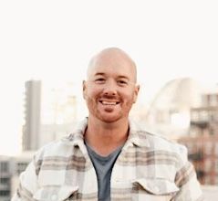 A bald man in a plaid shirt is smiling for the camera.