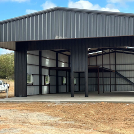 Open-air metal building with glass walls and a gravel foreground