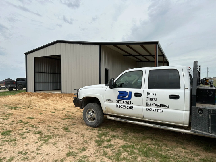 White work truck parked beside a metal warehouse on a dirt lot under cloudy sky.