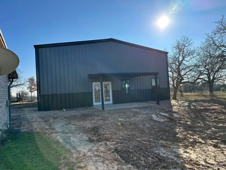 Small metal building with a front door and windows on a sunny rural lot.