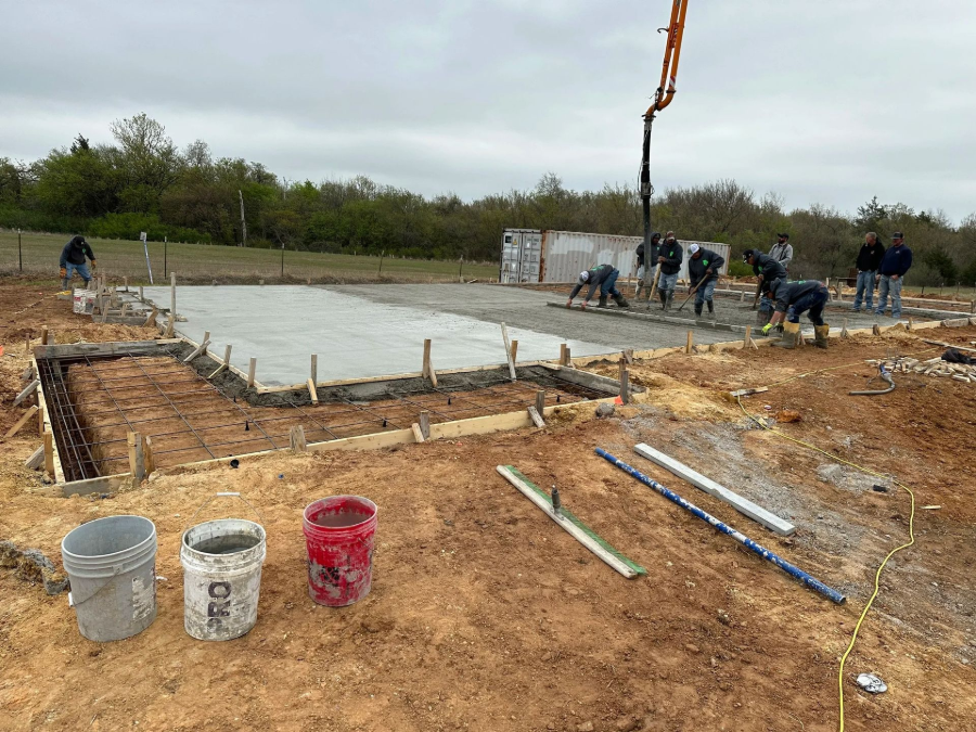 Construction site with concrete foundation forms, workers in the distance, and tools on a dirt lot
