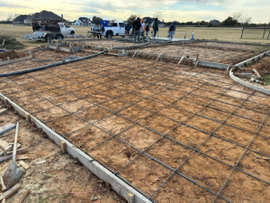 Construction site with rebar grid and concrete formwork laid out on the ground, workers in the distance