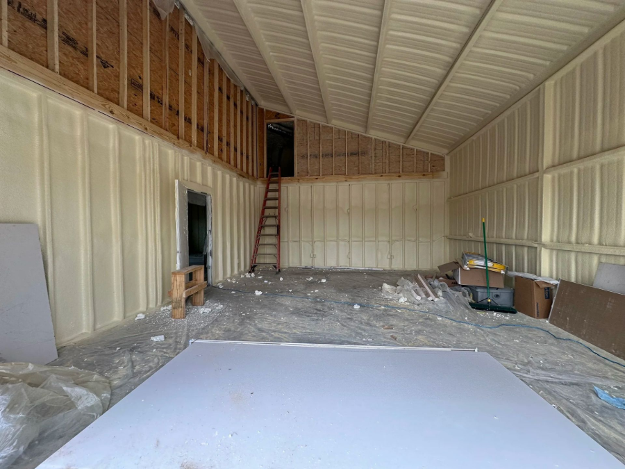 Unfinished insulated metal barn interior with ladder, workbench, and materials on the floor