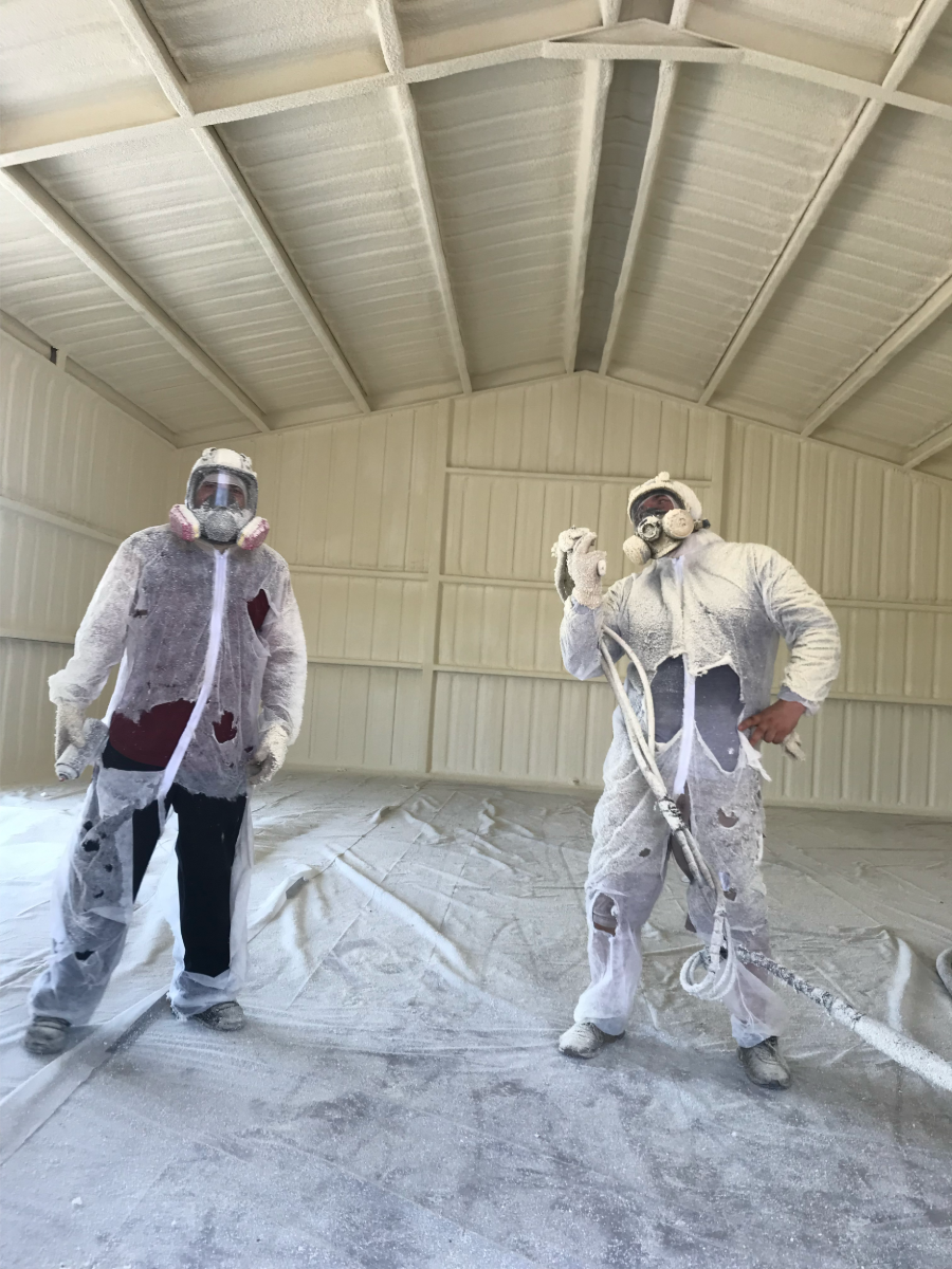 Two painters in white coveralls standing in a white-walled room, one holding a spray gun.