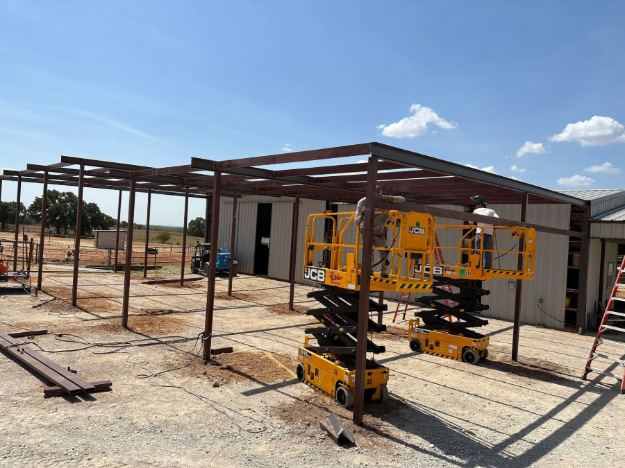 Construction site with steel frame, modular building, and yellow scissor lift under a blue sky