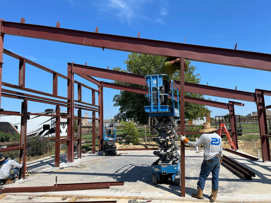 Workers erecting a steel building frame with a lift at an outdoor construction site