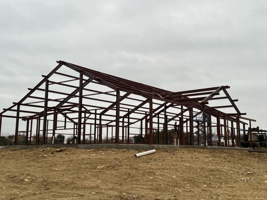 Partially built steel frame building on a dirt lot under a cloudy sky