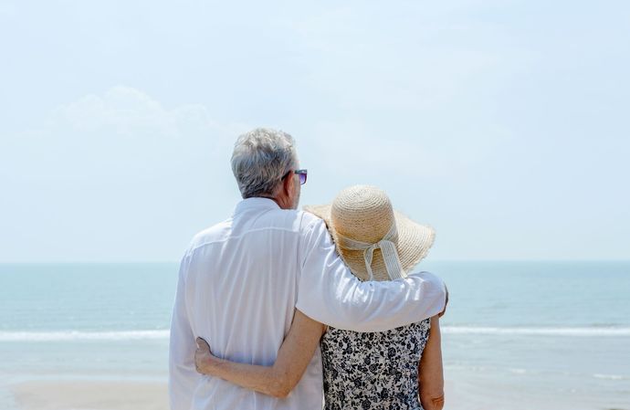 Two people embracing on a beach, facing the ocean under a clear sky.