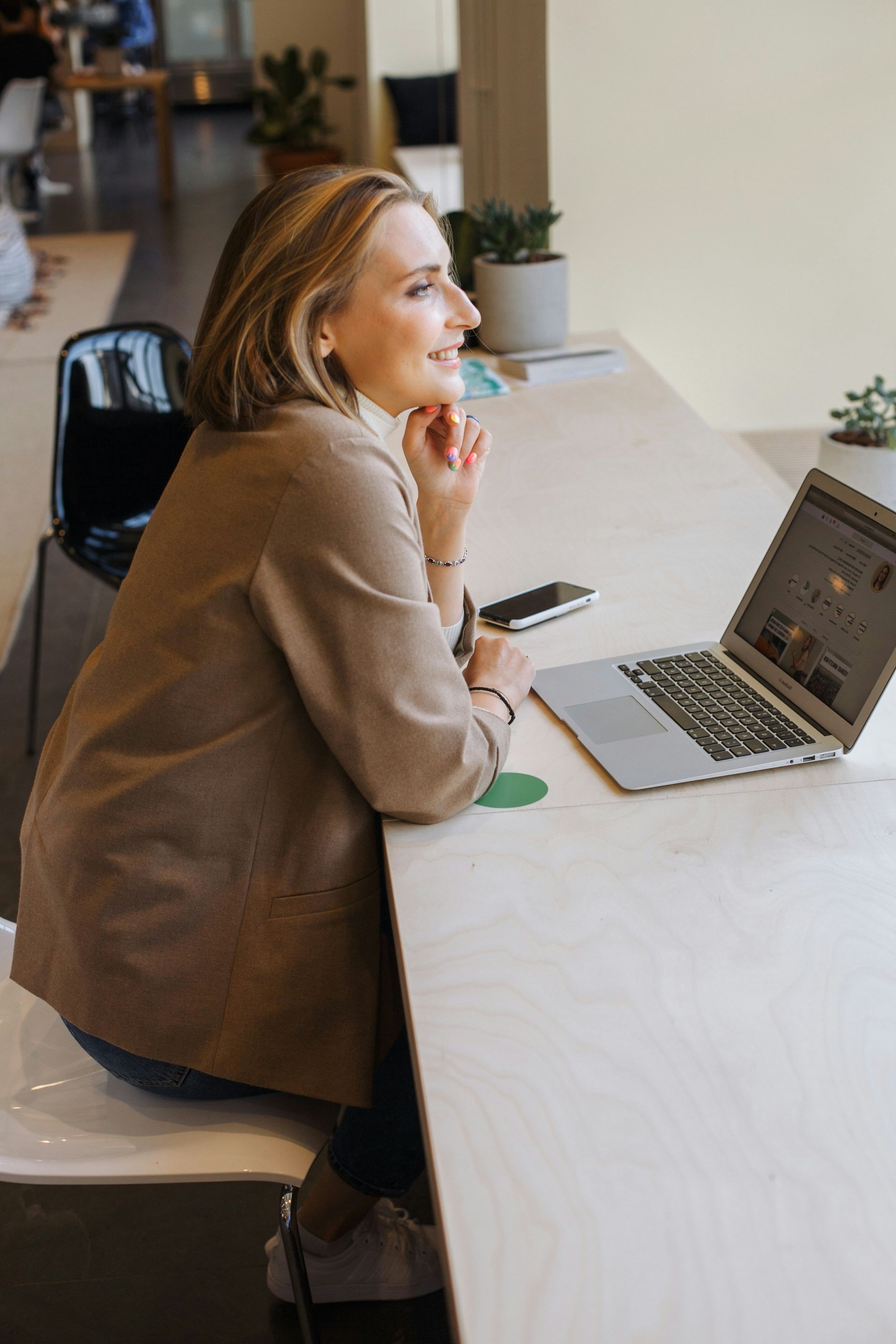Person sitting at a café table, smiling while using a laptop and phone