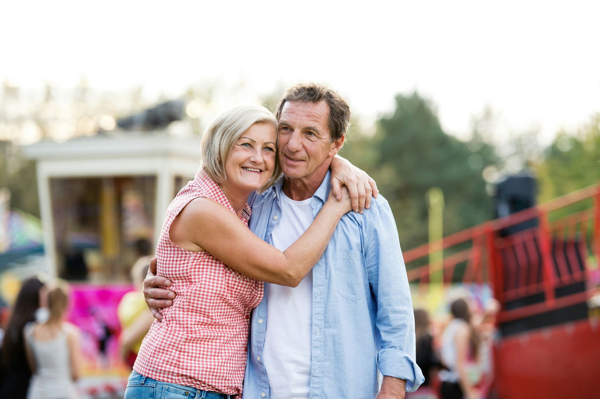 Smiling couple hugging outdoors at a fair with colorful rides in the background