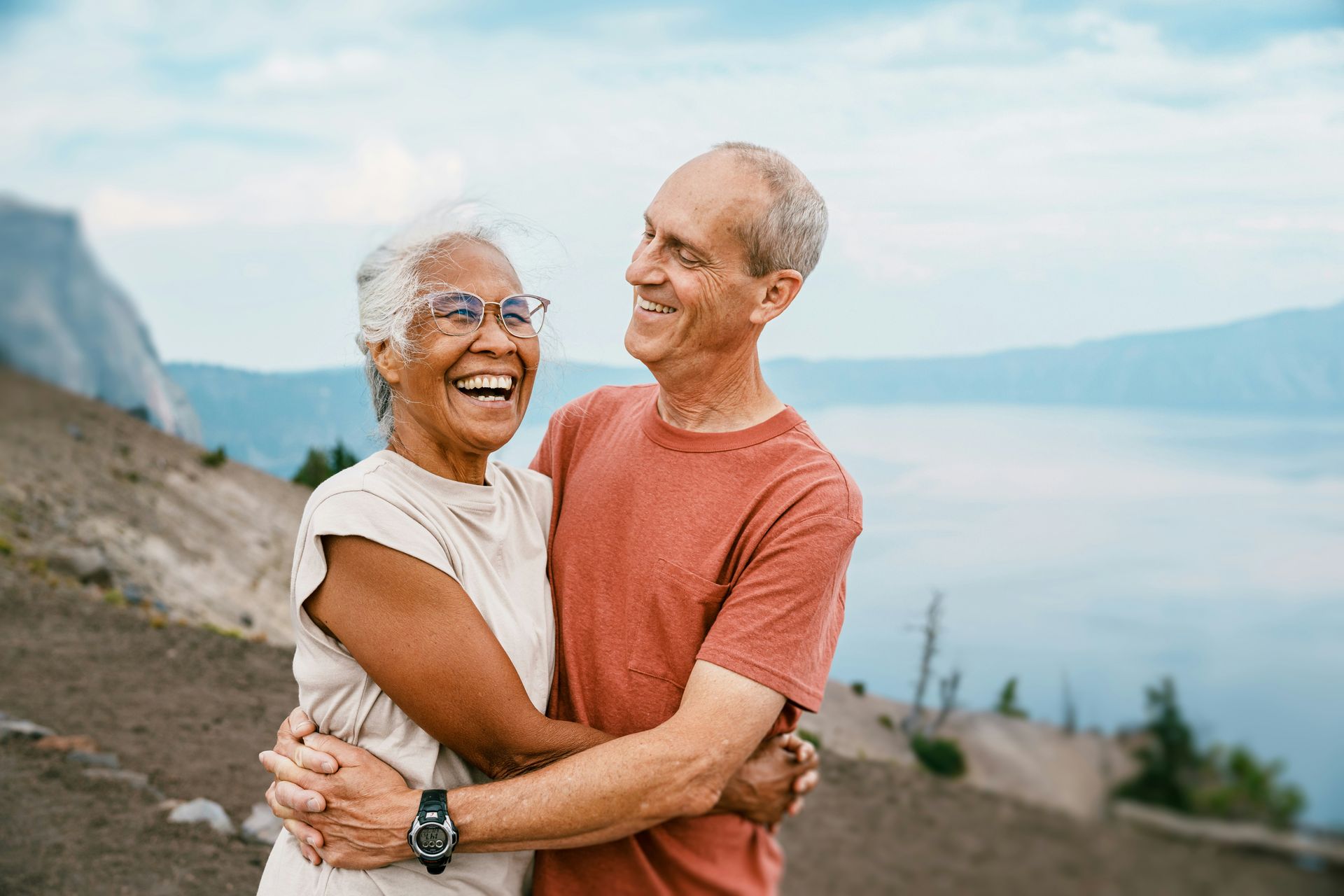 Two smiling people hugging on a coastal overlook with ocean and cliffs in the background