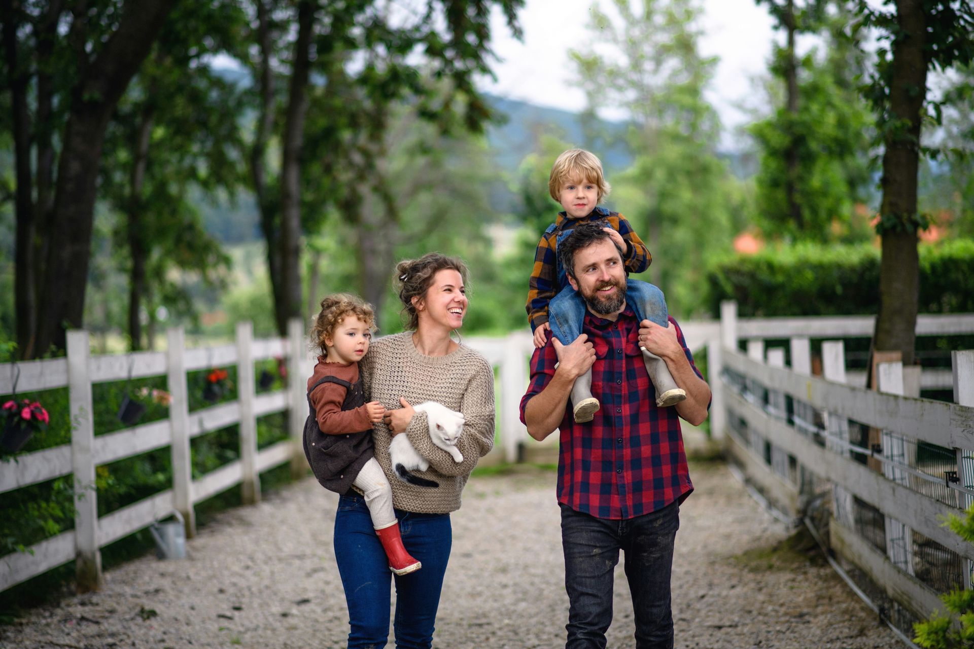 Family walking on a wooden bridge in a wooded park, with two children riding on adults’ shoulders.