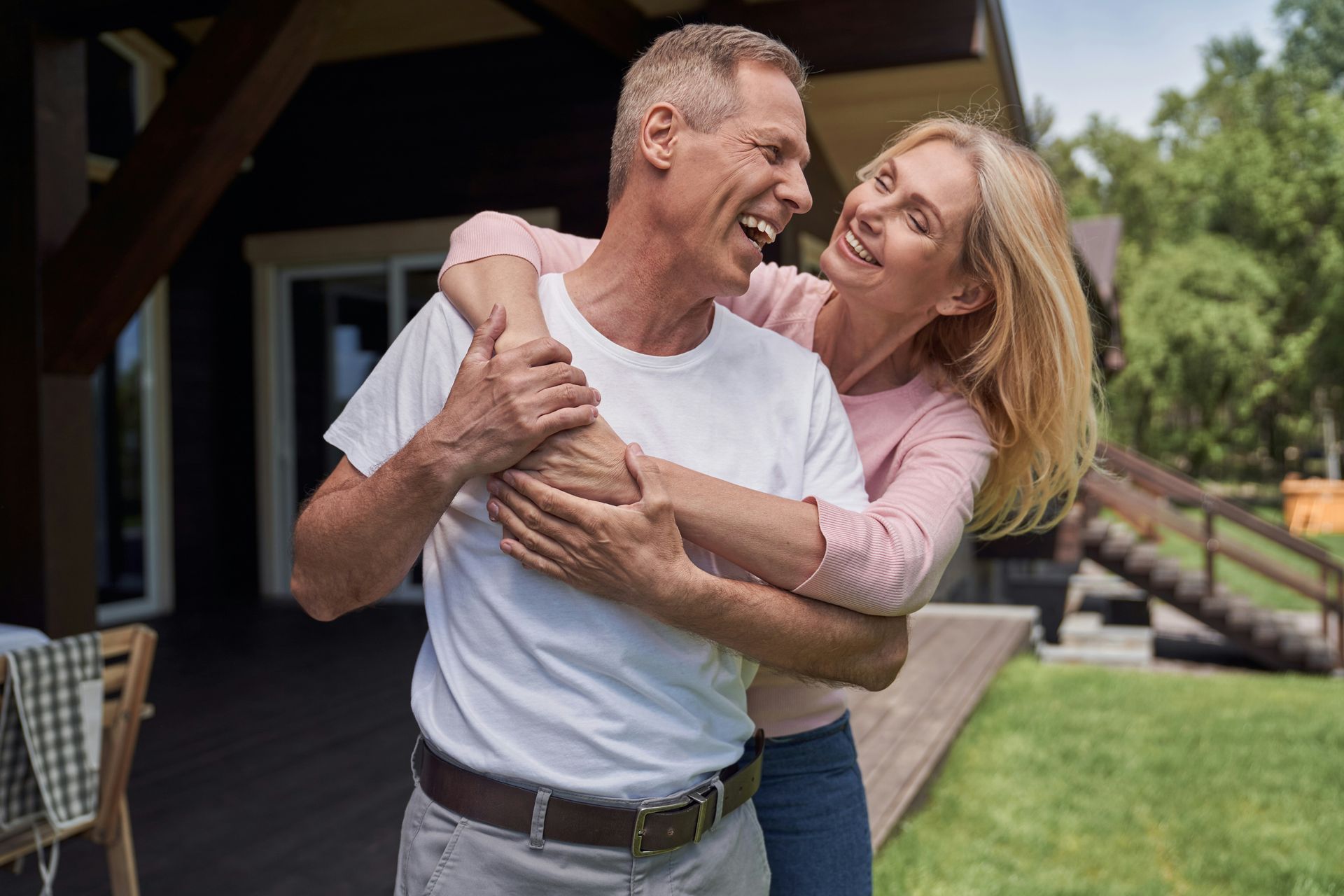 Two people laughing and embracing outside a house on a sunny day