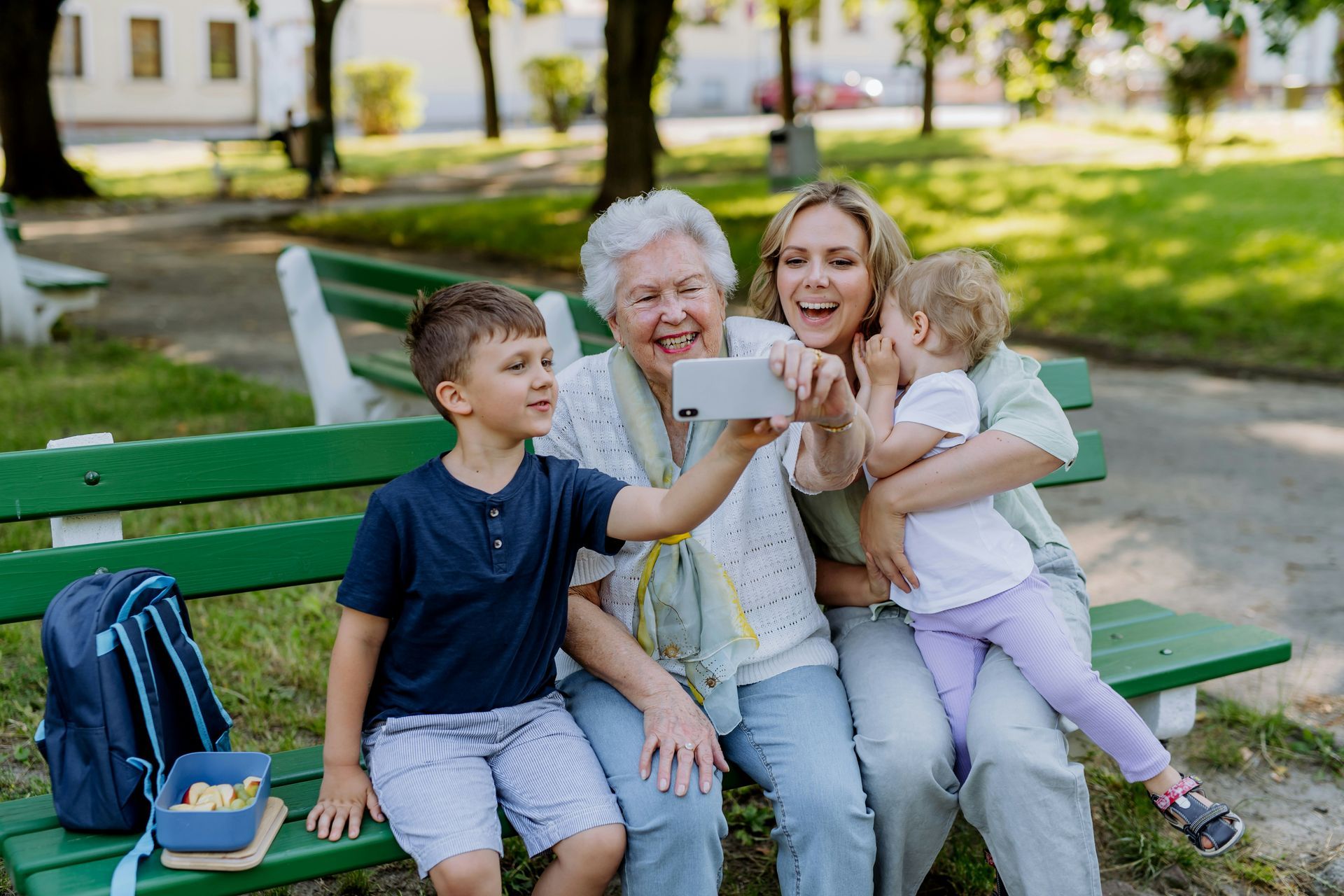 Three people on a park bench taking a selfie, with a blue backpack beside them.