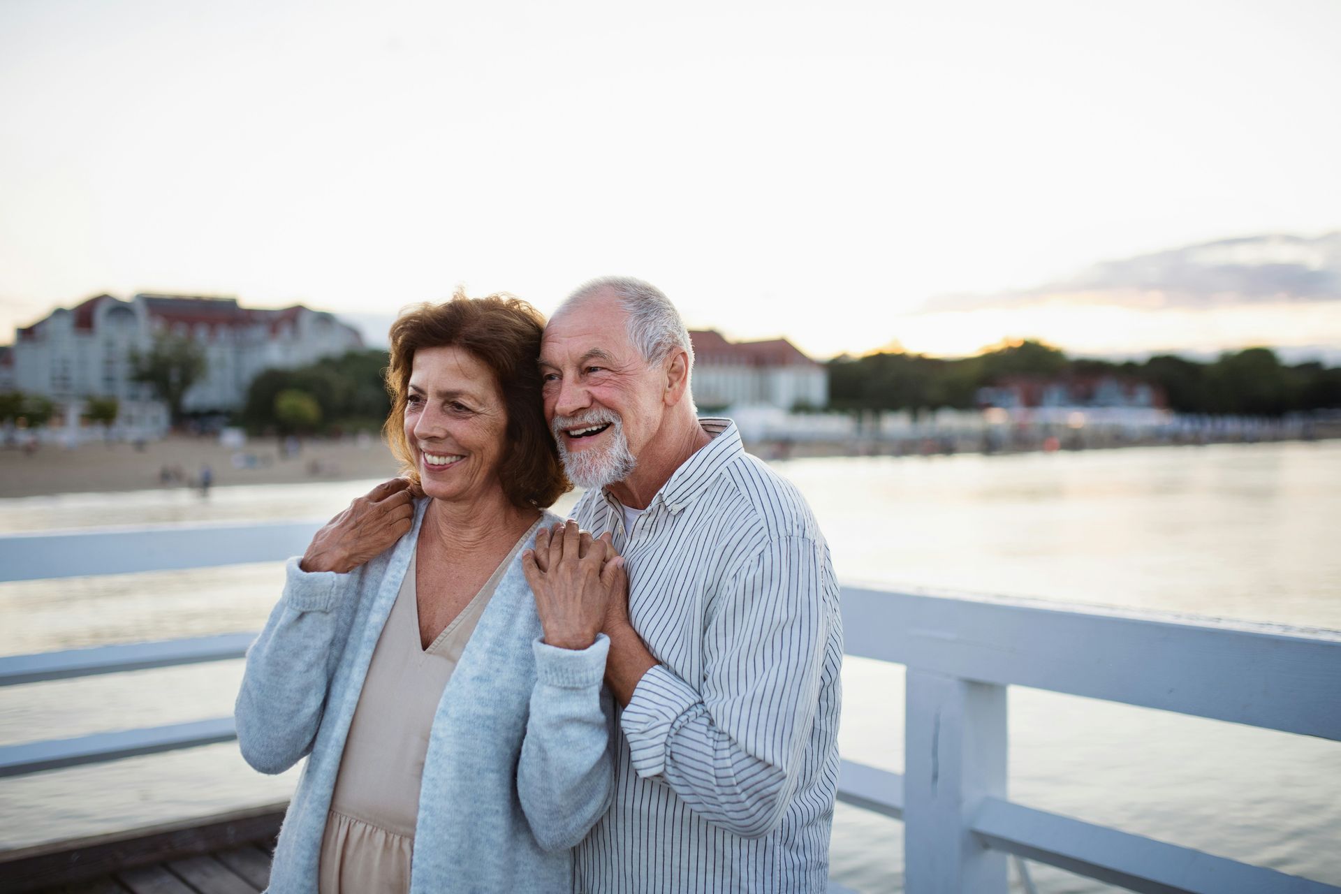 Smiling couple leaning on a white railing by the water at sunset