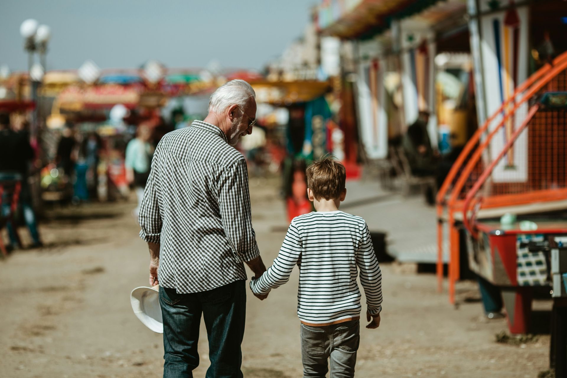 Two people walking hand in hand through a market street with colorful stalls and red structures