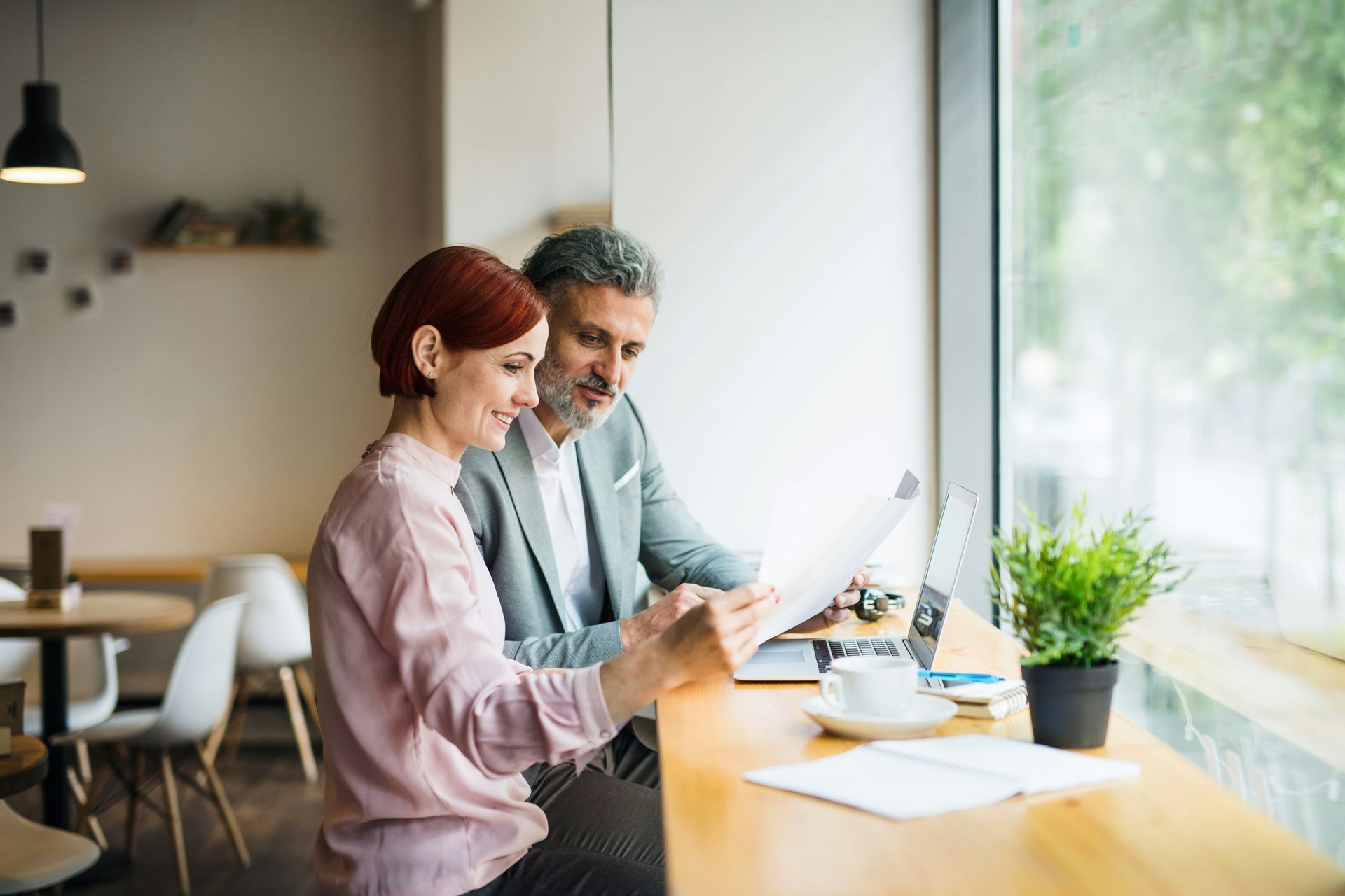 Two coworkers reviewing a laptop by a bright window in a modern office