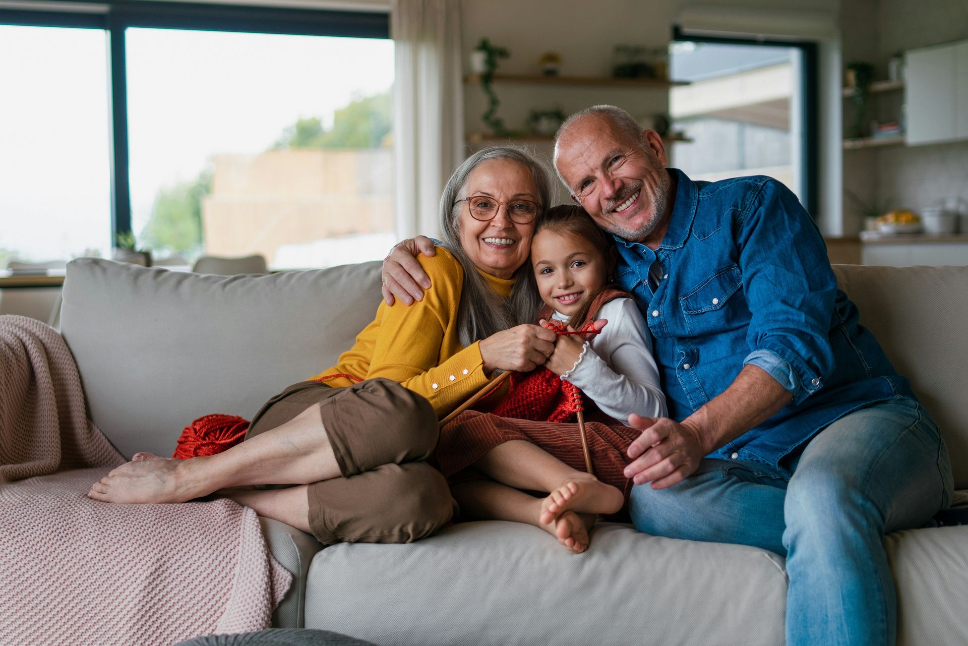 Three people sitting on a couch, smiling and hugging in a bright living room