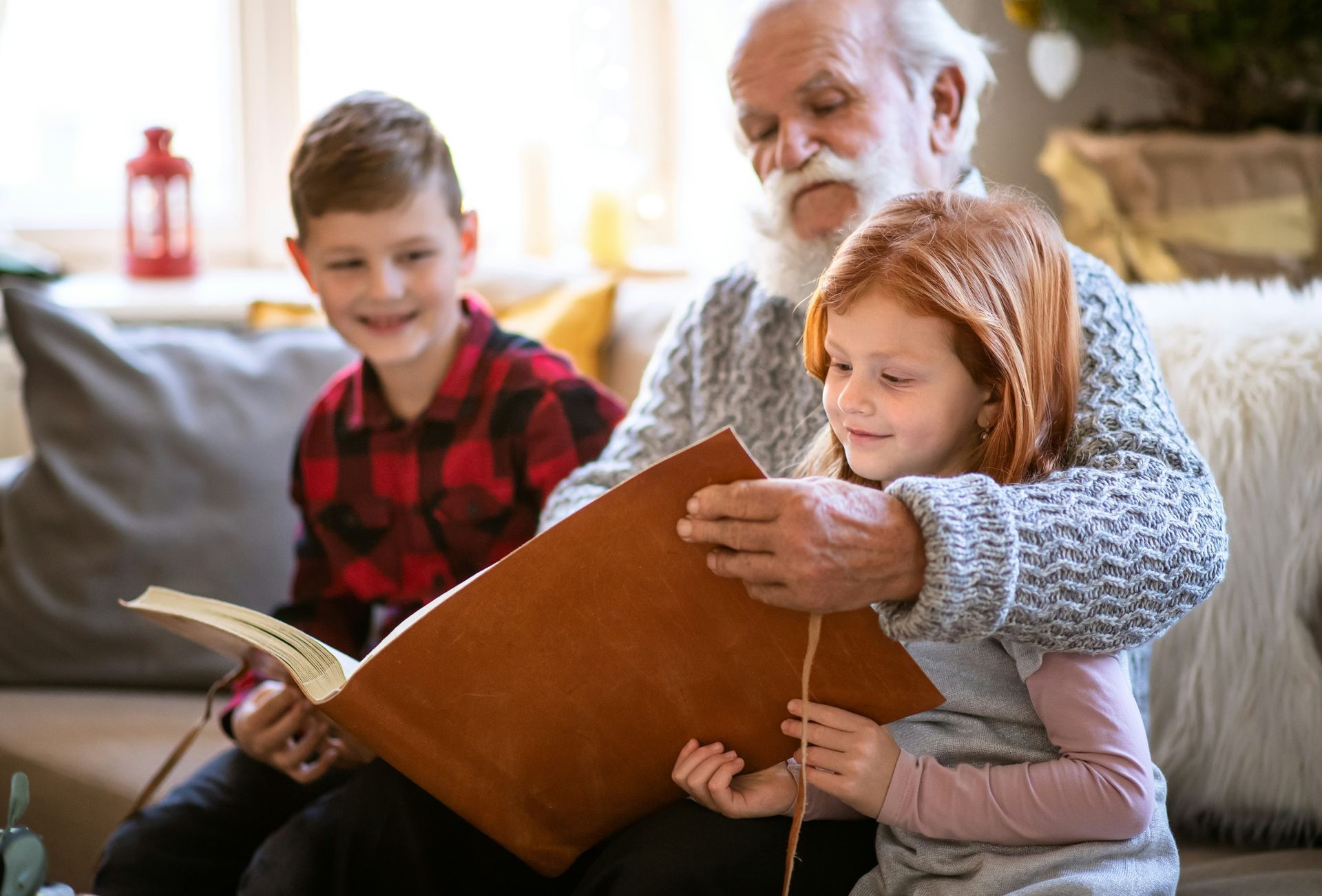 Three people reading a book together on a couch in a cozy living room