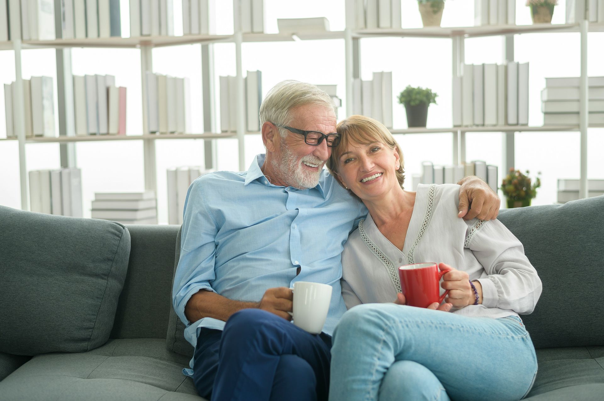 Two people cuddling on a couch, smiling with mugs in a bright living room
