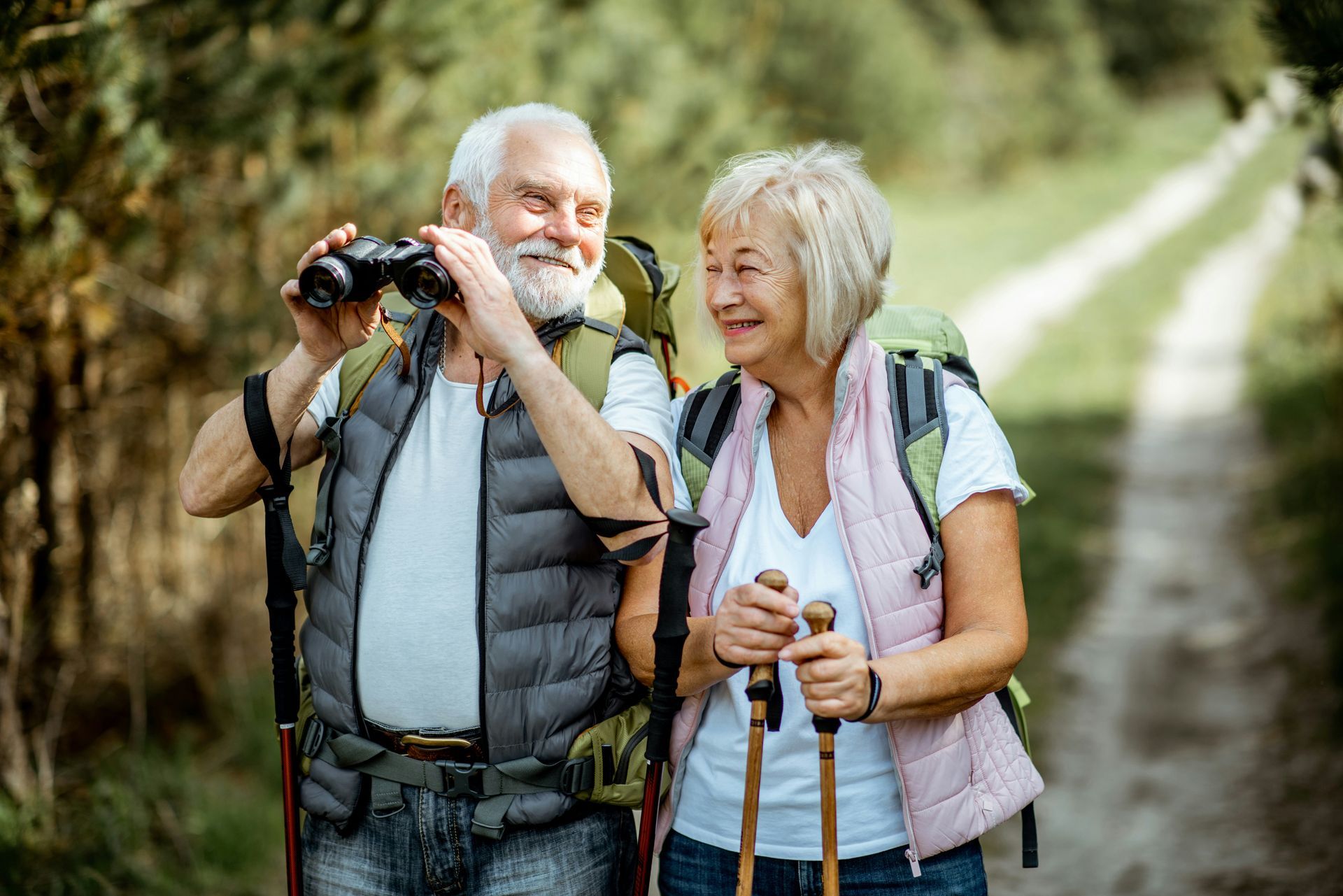 Two hikers on a forest trail, smiling and using trekking poles and a camera