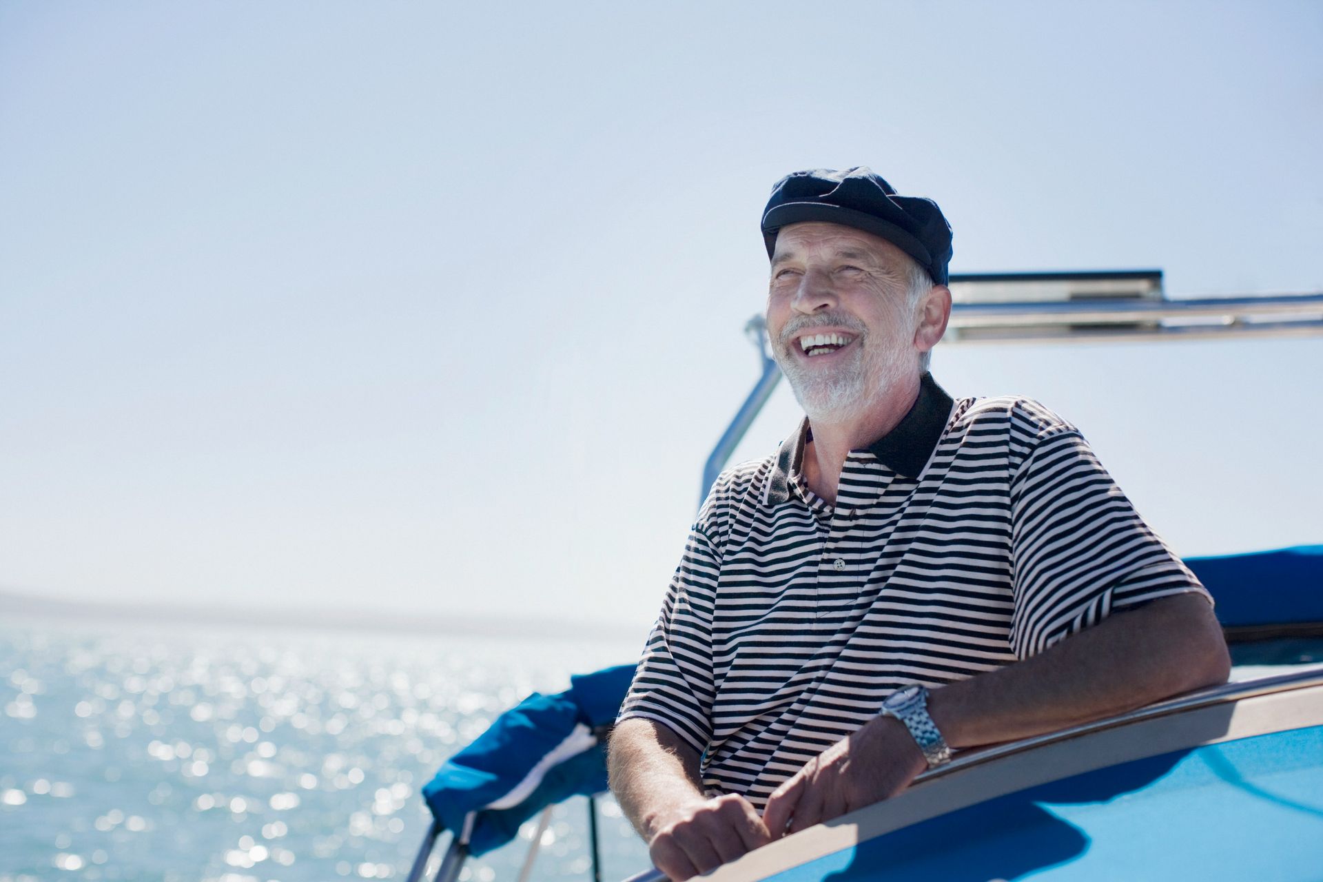 Smiling man in a striped shirt on a boat, with bright blue water and sky in the background