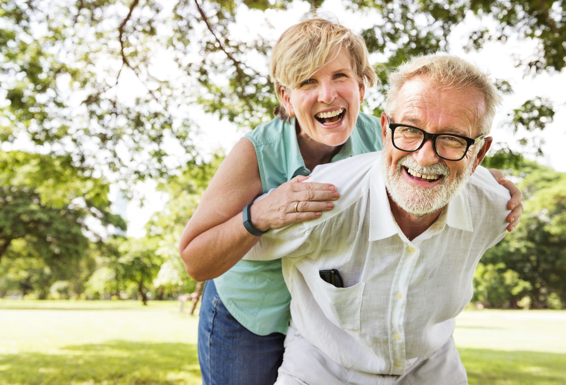 Smiling couple outdoors, with one giving the other a piggyback ride in a sunny park.