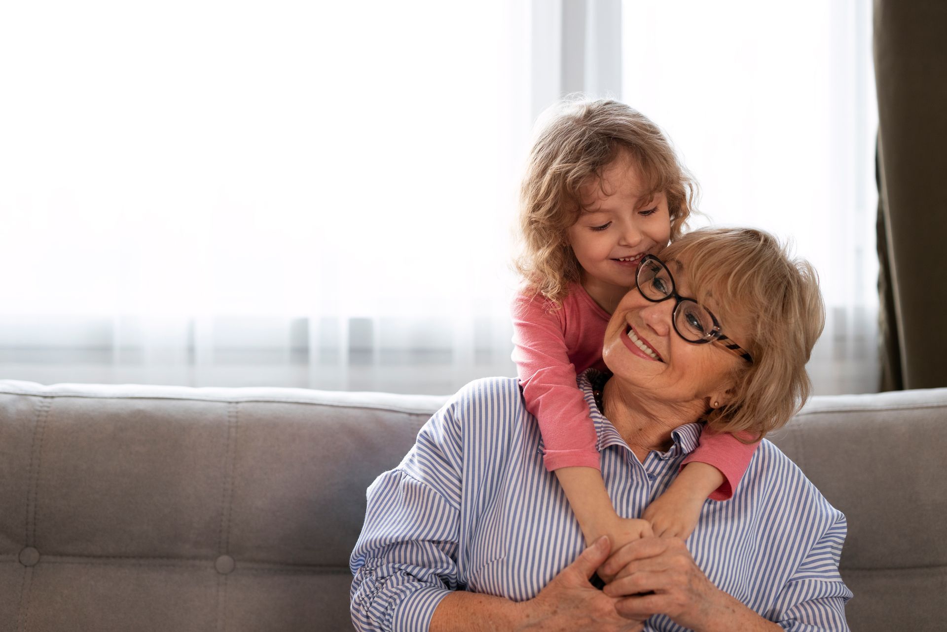 Smiling child hugging an older person on a couch near a bright window