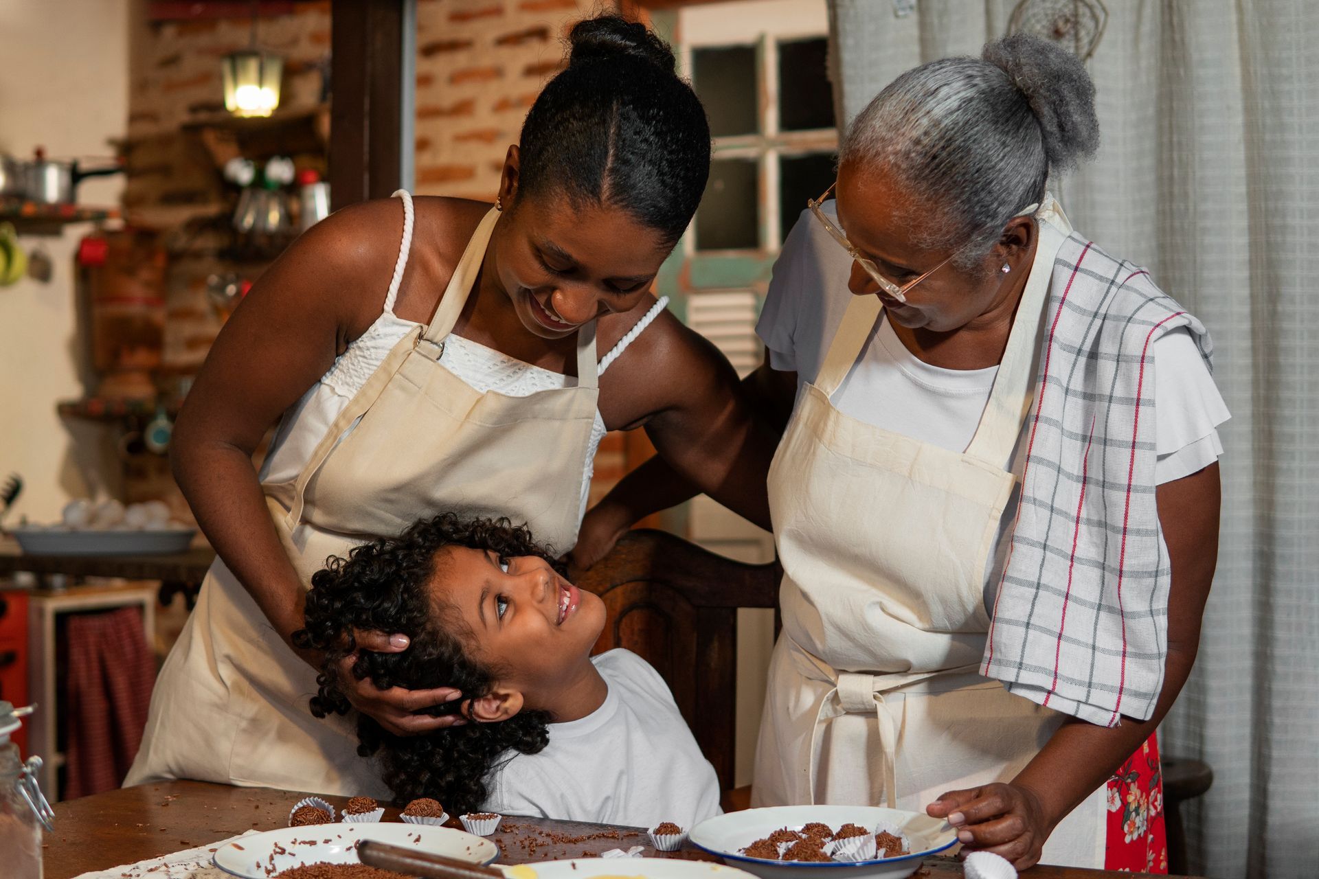 Two women in aprons styling a person's hair in a kitchen, with bowls on the table.