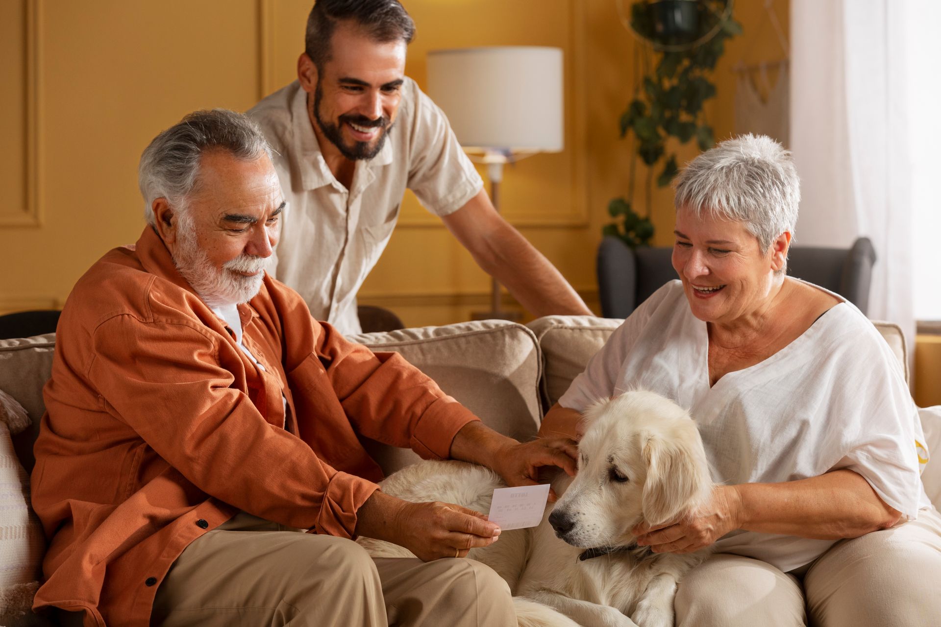 Three adults on a couch with a fluffy white dog in a cozy living room