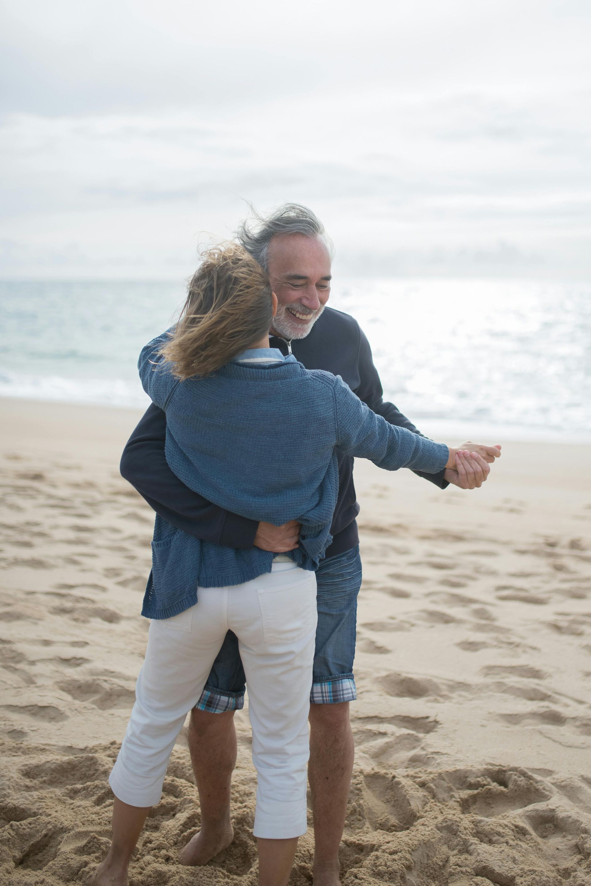 Couple hugging on a beach, with the ocean in the background.