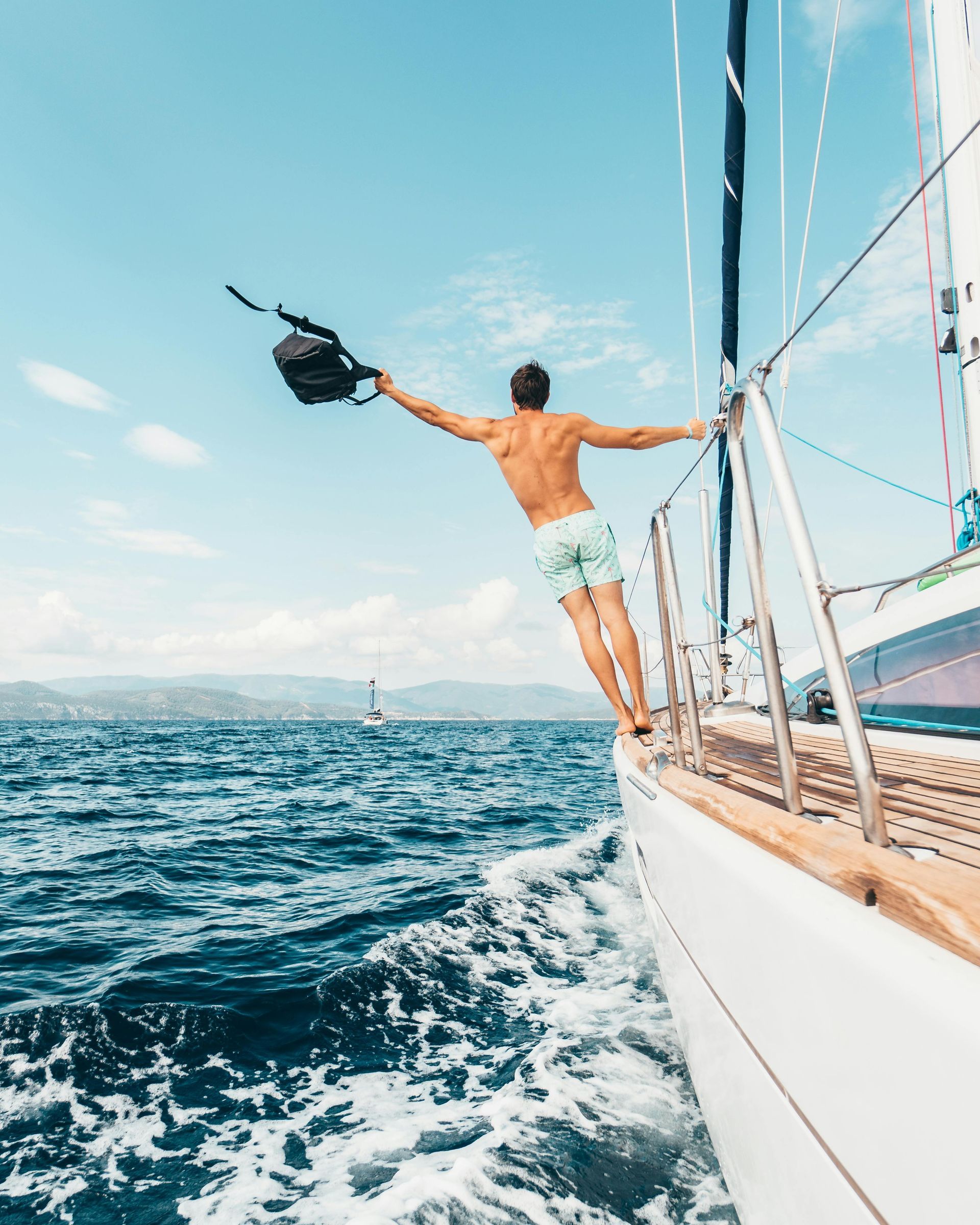 Person hanging off a sailboat with arms out over choppy blue water on a sunny day