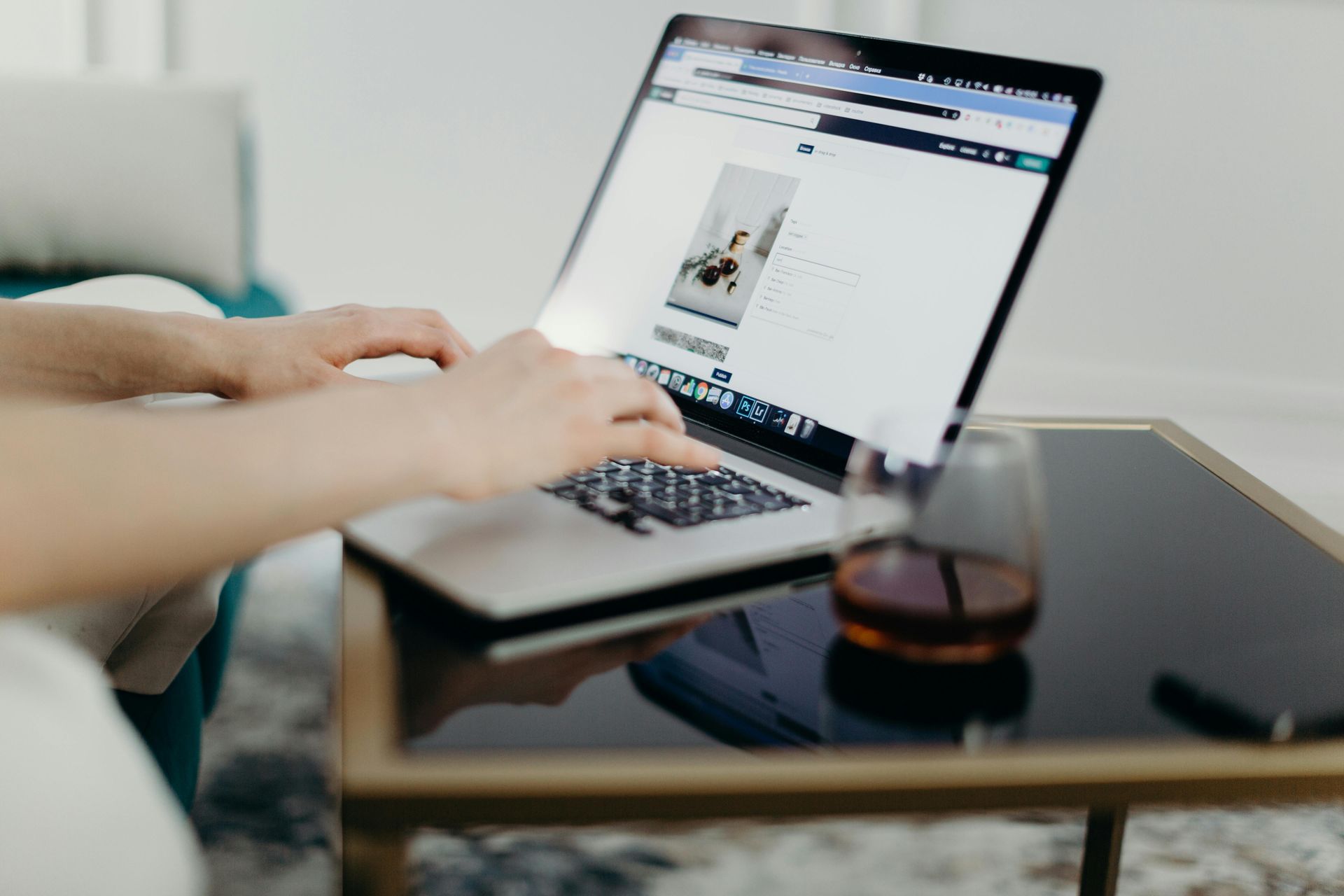 Person typing on a laptop at a glass table with a drink nearby