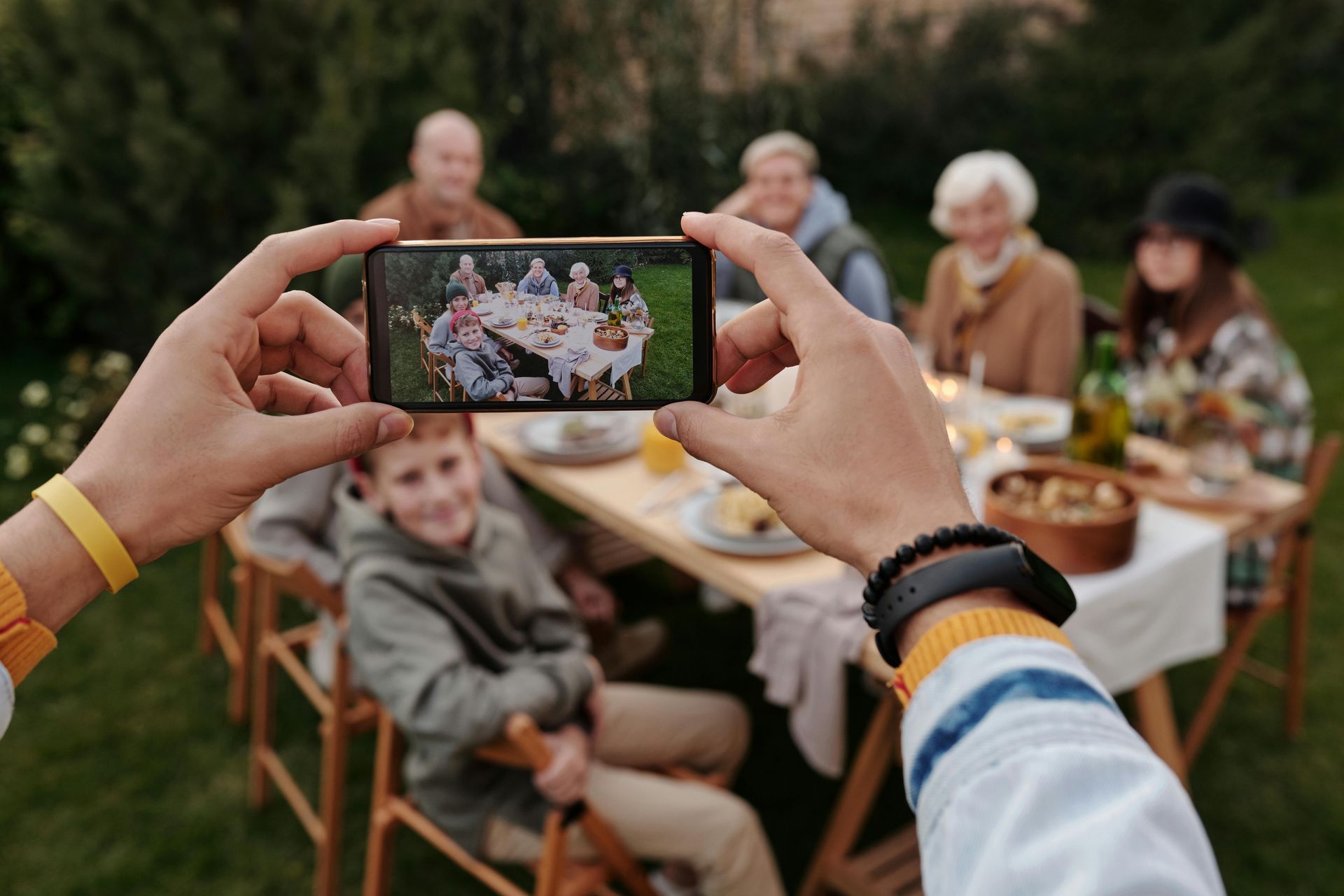 Hands taking a smartphone photo of a family seated around an outdoor table.