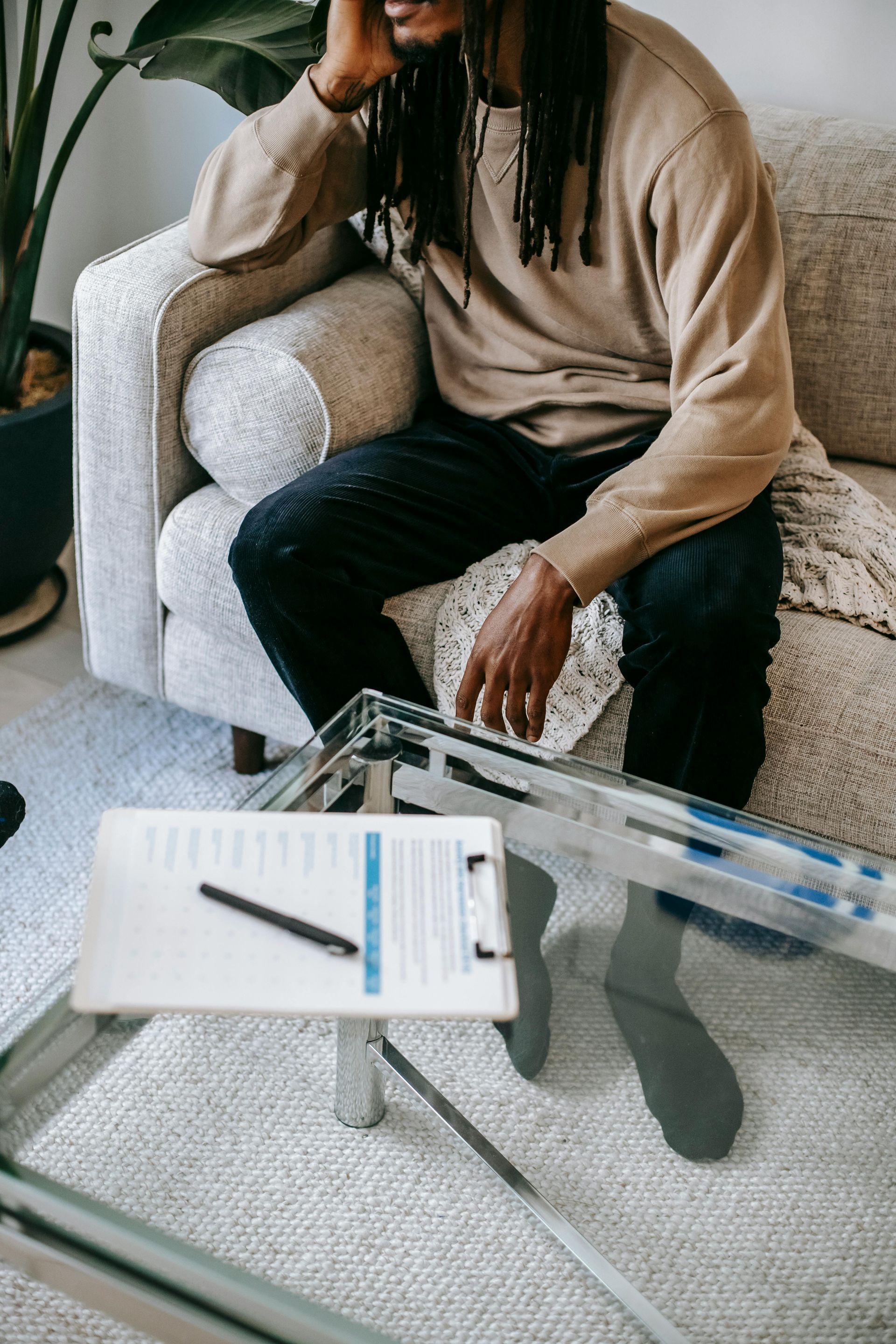 Person seated on a sofa beside a glass coffee table with a notebook and pen