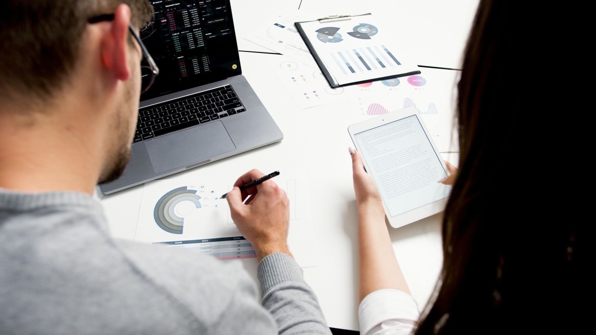 Two people at a desk reviewing charts and taking notes during a business meeting.